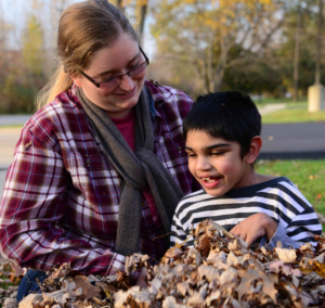 A young boys explores a pile of autumn leaves with his teacher.