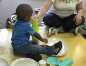 A toddler and an adult play with stacking plates and cups.